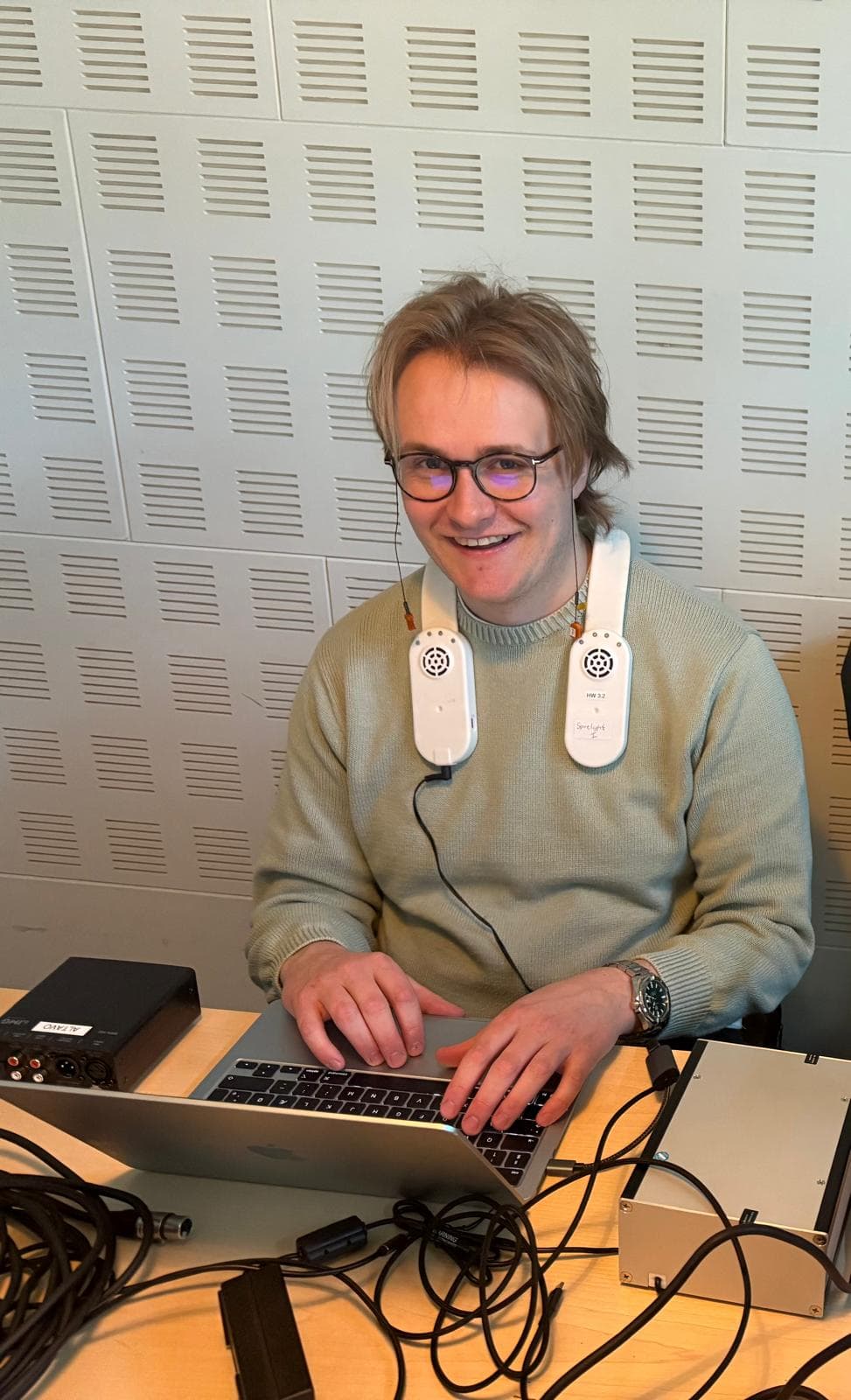 A researcher at a desk in a sound-treated room, wearing the sensor unit used in the two Altavo sessions, with recording hardware on the desk